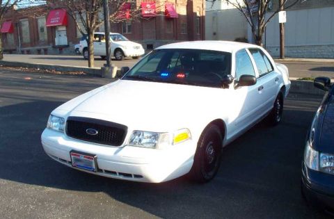 1998 Ford Crown Victoria - White police car with lights on the dash is parked next to another vehicle.