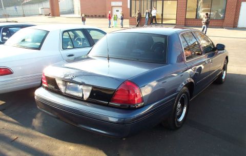 1998 Ford Crown Victoria - Two Ford Crown Victorias parked outside a brick building.