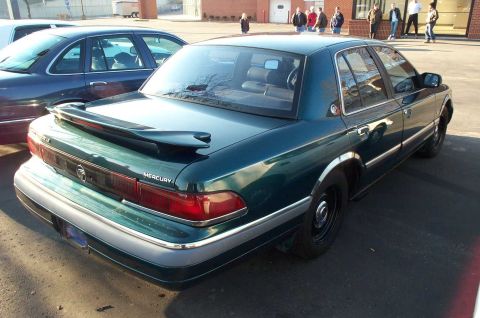 1998 Ford Crown Victoria - A dark green Mercury Grand Marquis is parked next to another car.