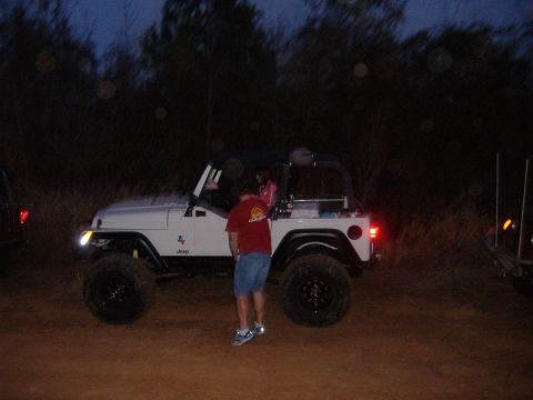 2004 Jeep Wrangler - A white Jeep Wrangler with off-road tires is parked on a dirt path at dusk, with a person standing next to it.