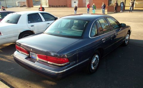 1998 Ford Crown Victoria - Two Ford Crown Victorias parked outside a building with people standing in the background.