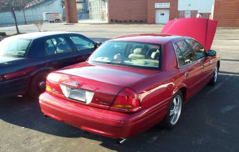 1998 Ford Crown Victoria - Two sedans are parked side-by-side, one with its hood open, in an outdoor lot.