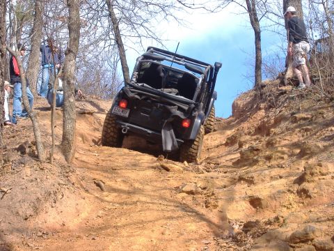 2004 Jeep Wrangler - A black Jeep Wrangler TJ navigates a challenging off-road trail with spectators watching from the side.