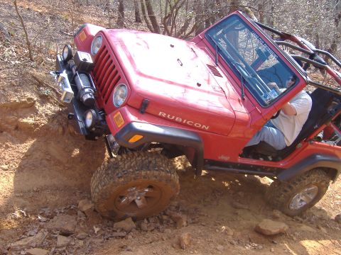 2004 Jeep Wrangler - A red Jeep Wrangler Rubicon navigates a steep, muddy incline during an off-road excursion.