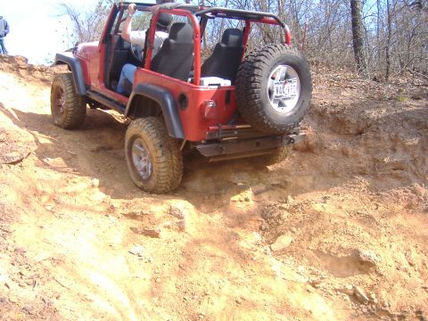 2004 Jeep Wrangler - A red Jeep Wrangler navigates a steep, dusty trail with a spare tire mounted on the back.