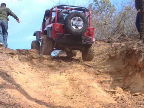 2004 Jeep Wrangler - A red Jeep Wrangler navigates a challenging off-road trail with steep inclines and loose dirt.