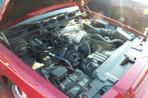 1998 Ford Crown Victoria - The engine bay of a red 1998 Ford Crown Victoria is shown, with another vehicle partially visible in the background.