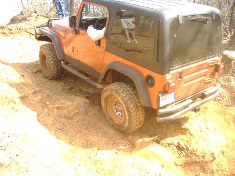 2004 Jeep Wrangler - Orange Jeep TJ navigating a challenging off-road trail with steep inclines and loose dirt.