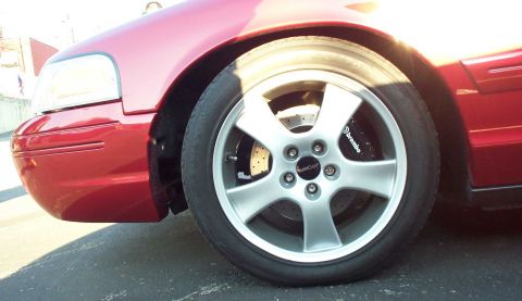 1998 Ford Crown Victoria - Close-up of a red 1998 Ford Crown Victoria's front wheel and fender, showing aftermarket Brembo brakes.