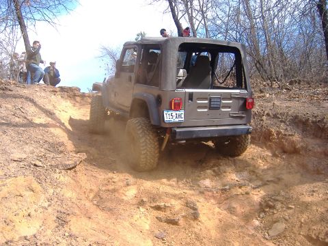 2004 Jeep Wrangler - A brown Jeep Wrangler navigates a steep, dusty off-road trail with onlookers watching.