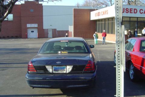 1998 Ford Crown Victoria - A dark blue 1998 Ford Crown Victoria is parked in front of a used car dealership, displaying a Steelers sticker on the rear window.