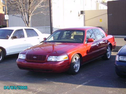 1998 Ford Crown Victoria - A red sedan is parked in a lot next to a white sedan, with a building in the background.