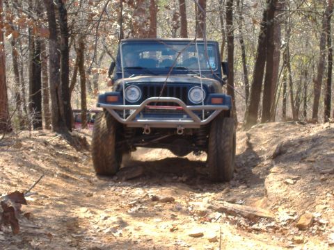 2004 Jeep Wrangler - A dark blue 2004 Jeep TJ is shown from the front as it drives over a challenging, rocky off-road trail.