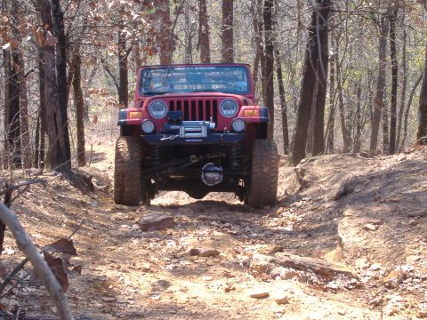 2004 Jeep Wrangler - A red Jeep Wrangler navigates a challenging off-road trail through a forest.