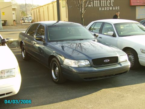 1998 Ford Crown Victoria - Two Ford Crown Victorias parked outside a building with 'Zimmer Hardware' signage.
