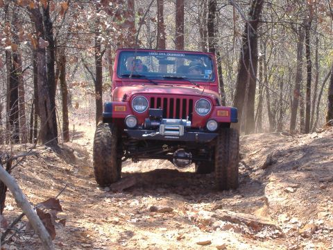 2004 Jeep Wrangler - A red Jeep Wrangler navigates a rocky, wooded trail.