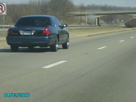 1998 Ford Crown Victoria - A dark sedan is seen from behind driving on a highway with a date stamp of 04/03/2006.