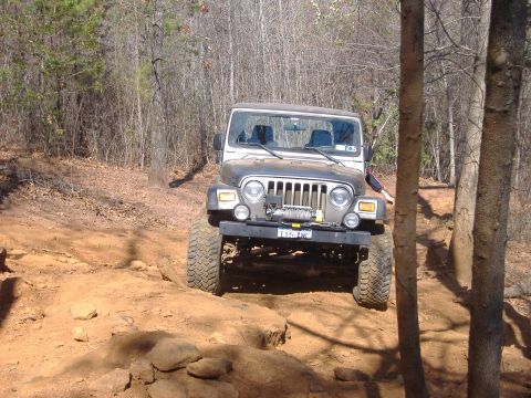 2004 Jeep Wrangler - A silver Jeep TJ drives on a dirt trail surrounded by trees.