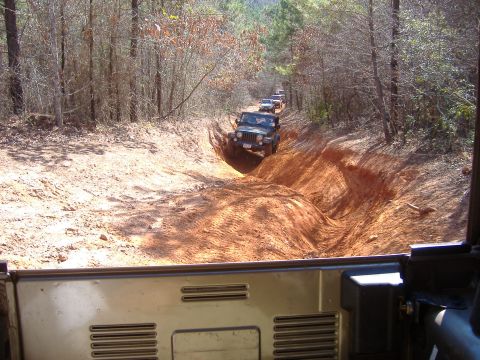2004 Jeep Wrangler - A line of Jeeps navigates a challenging off-road path through a wooded area.