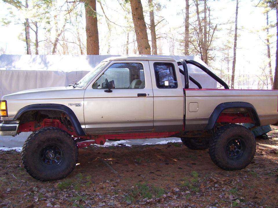 Lifted tan Ford Ranger extended-cab pickup on large tires in woods