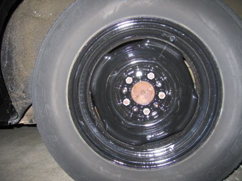 1991 Ford LTD Crown Victoria - Goodyear Eagle GT tire on a painted black steel wheel, showing exposed lug nuts and a rusty hub.