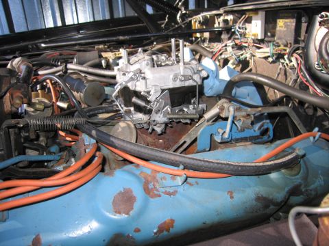 1991 Ford LTD Crown Victoria - open engine bay showing a chrome four-barrel carburetor atop a light-blue V8 engine block with orange plug wires and tangled hoses.