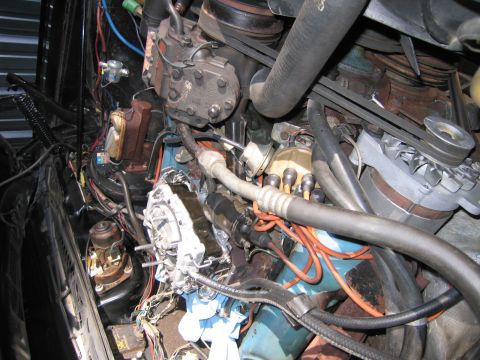 1991 Ford LTD Crown Victoria - cluttered engine compartment with a chrome carburetor, black A/C compressor and accessory belts mounted on a blue V8 engine.