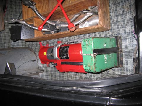 1991 Ford LTD Crown Victoria - red fire extinguisher and a green metal first-aid kit stored in a car trunk lined with plaid-patterned material.