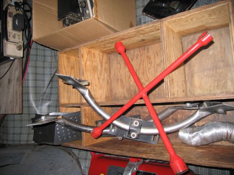 1991 Ford LTD Crown Victoria - red cross-style four-way lug wrench rests across a curved chrome part inside a sectioned plywood storage crate.
