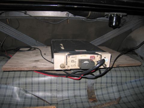 1991 Ford LTD Crown Victoria - vintage metal two-way radio transceiver mounted on a plywood board beneath a car, wired with red and black cables.