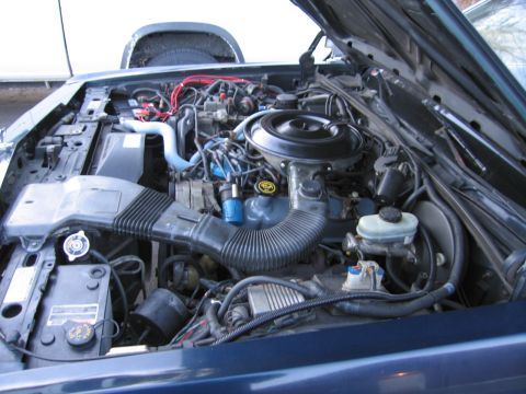 1991 Ford LTD Crown Victoria - The engine compartment of a car is shown with the hood raised, revealing various mechanical parts and systems.