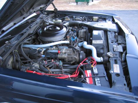 1991 Ford LTD Crown Victoria - The engine bay of a dark blue 1991 Ford Crown Victoria LTD is visible with the hood open, revealing the V8 engine and associated components.