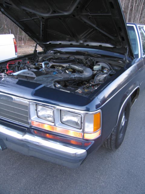 1991 Ford LTD Crown Victoria - The engine bay of a 1991 Ford Crown Victoria LTD is visible with the hood open, revealing the car's mechanical components.