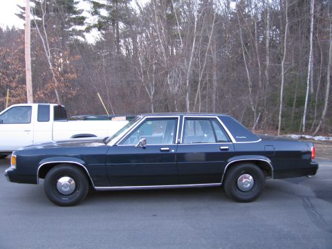 1991 Ford LTD Crown Victoria - A dark blue sedan is parked on an asphalt surface with a white truck in the background.
