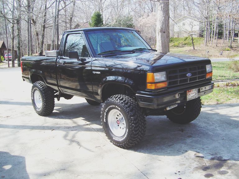 Black lifted Ford Ranger pickup on mud tires parked in a driveway