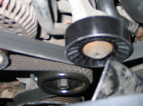 1994 Ford Bronco - Close-up inside an engine bay showing two newly installed black serpentine belt pulleys, a finned tensioner pulley above and a smaller smoo…