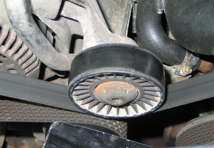 Worn serpentine-belt idler pulley with rusty center hub, seen from under the engine