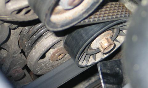 1994 Ford Bronco - Close-up inside an engine bay showing a ribbed serpentine belt wrapped around several pulleys, including a grooved pulley with surface rust…