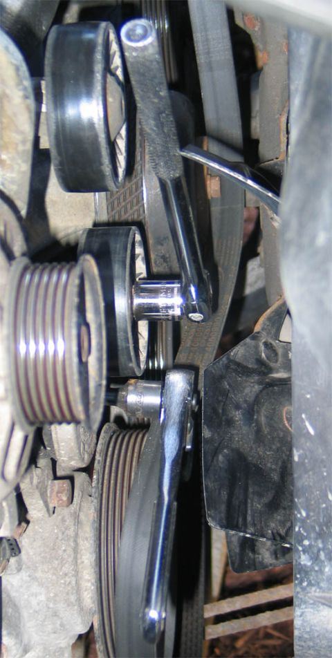 1994 Ford Bronco - Tight underhood shot of a serpentine belt drive with a chrome breaker bar and socket hooked onto the automatic belt tensioner pulley to rel…