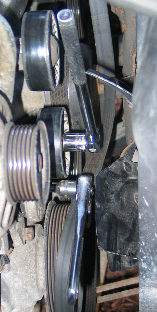 Breaker bar on a serpentine belt tensioner pulley in an engine bay