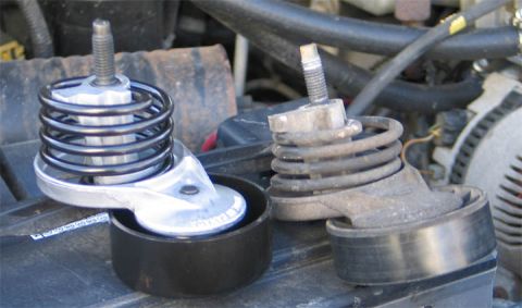 1994 Ford Bronco - Side-by-side comparison of two spring-loaded serpentine belt tensioners resting in an engine bay: a new unit with bright aluminum arm and c…