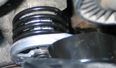 1994 Ford Bronco - Extreme close-up of an automotive serpentine belt tensioner assembly, showing a black coiled tension spring and a chrome/polished metal ten…