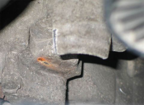 1994 Ford Bronco - Tight close-up under the hood of a cast-aluminum engine mounting boss with a stepped bracket pad, showing surface grime and an orange paint…