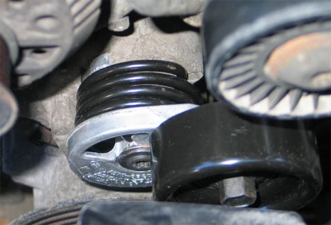1994 Ford Bronco - Extreme close-up of a serpentine belt tensioner installed on an engine, showing the cast aluminum body, exposed coil spring and the black t…