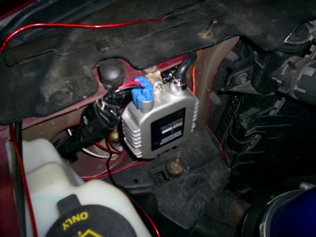 Vacuum pump and oil bottle wedged in engine bay near coolant reservoir