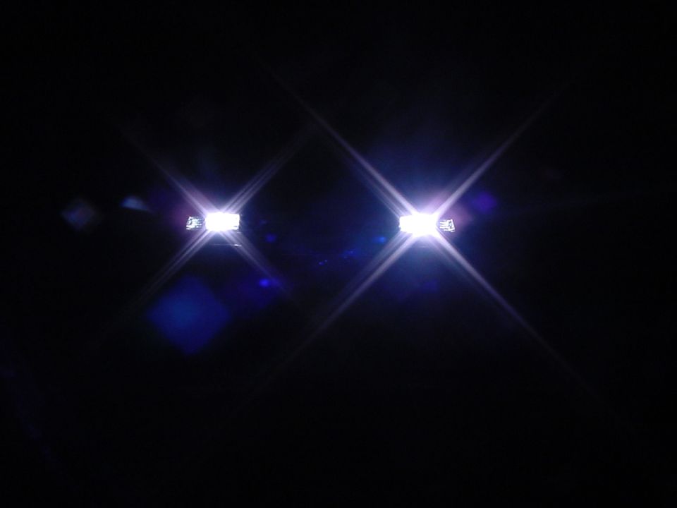 Two bright white headlights glowing in total darkness with lens-flare stars