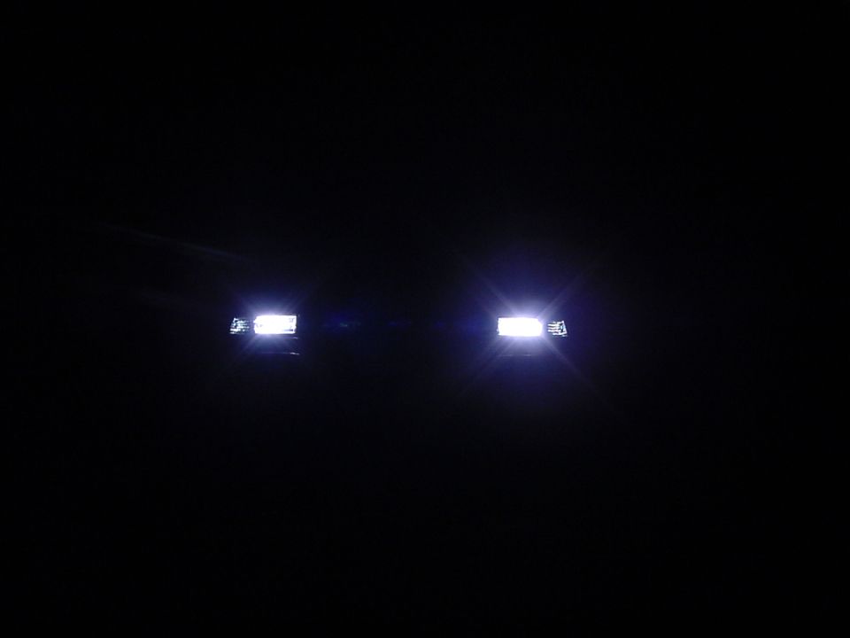 Two white headlights lit far apart in darkness, faint blue tint