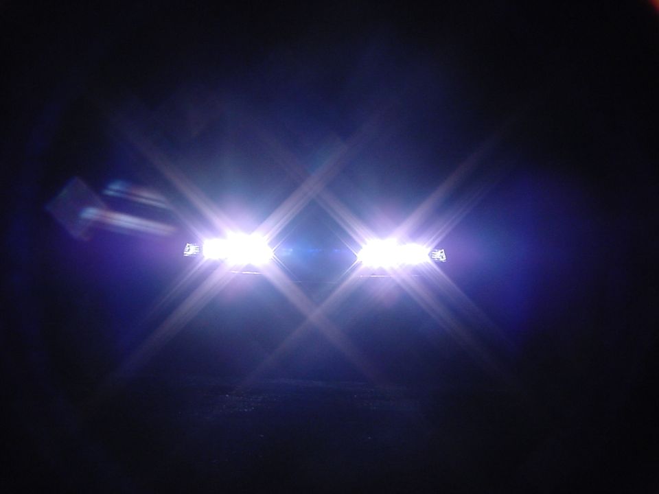 Two close-set white headlights glaring in darkness with bright flare stars