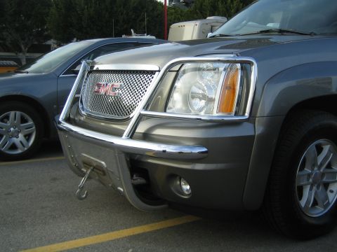 1990 Ford Bronco - Angled front-corner view of a gray GMC SUV with chrome grille guard and fog lights in a parking lot.