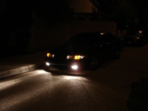 1993 Ford Taurus - A dark sedan is parked on a street at night, its headlights and foglights illuminating the road.
